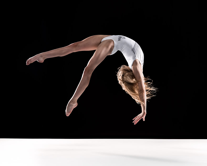 Gymnast in a strong finishing position on a dark studio backdrop